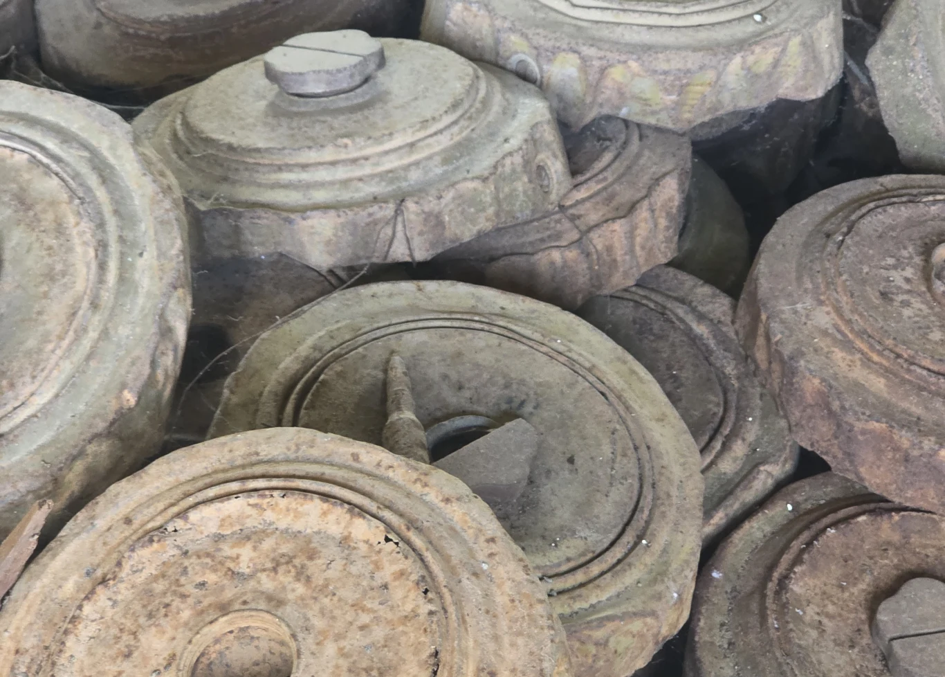 Stos zardzewiałych min przeciwpancernych ustawionych jedna na drugiej, wyraźnie widoczne metalowe obudowy oraz charakterystyczne pokrętła i okrągłe kształty, całość pokryta nalotem rdzy i kurzem.