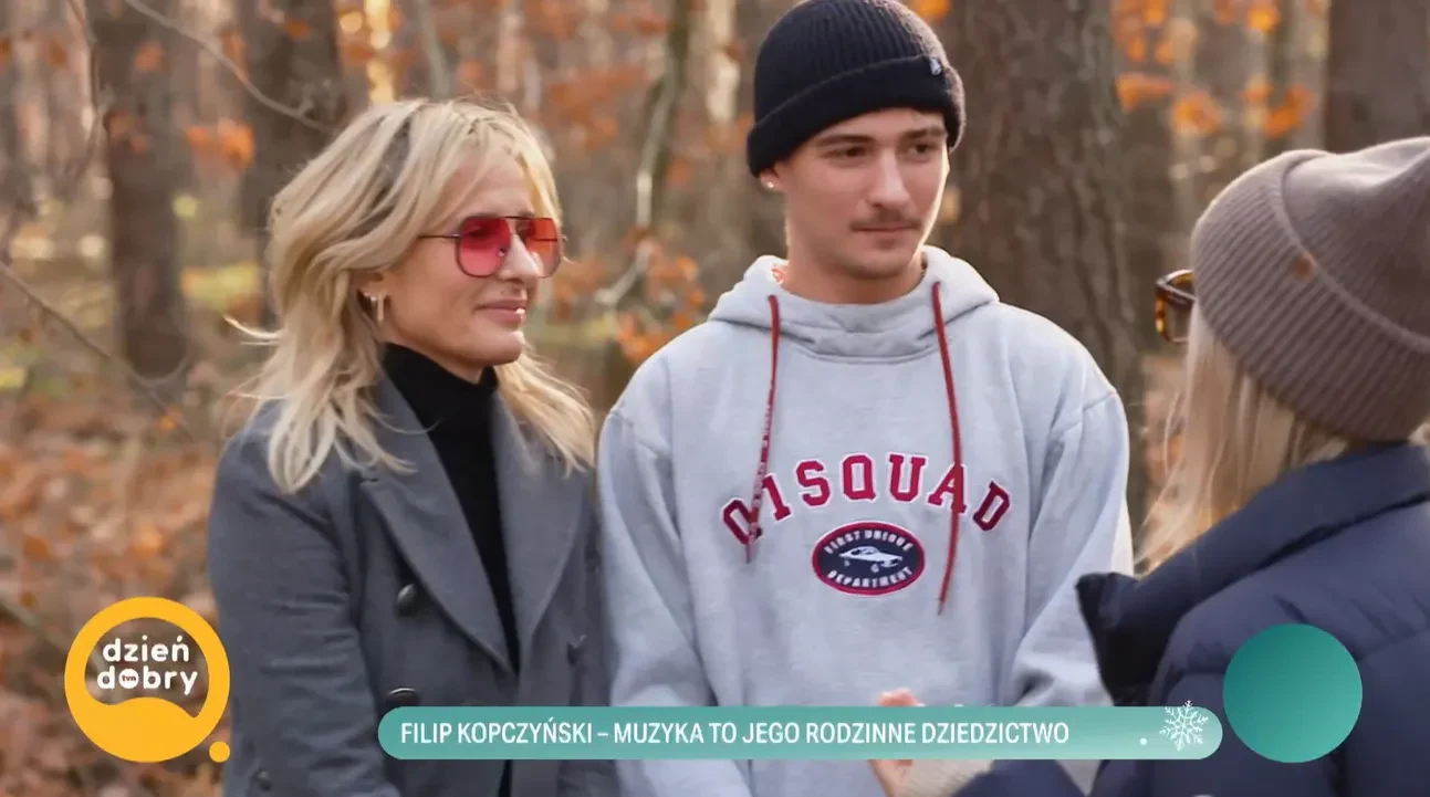 Trzy osoby rozmawiają ze sobą w lesie, jedna z kobiet ma jasne włosy i czerwone okulary, obok niej stoi młody mężczyzna w szarej bluzy z napisem i czarnej czapce, naprzeciwko nich ktoś w ciemnej kurtce i jasnych okularach. Jesienne liście na pierwszym ...