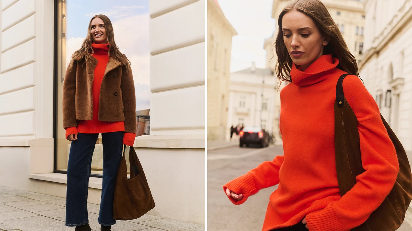 Swetry i kardigany, obowiązkowy element garderoby Młoda kobieta ubrana w jasnopomarańczowy sweter z wysokim kołnierzem, brązową kurtkę oraz ciemne dżinsy, nosząca dużą brązową torbę na ramieniu. Stoi na miejskim chodniku wśród jasnych budynków lub idzie ulicą w jasnym, dziennym świetle.