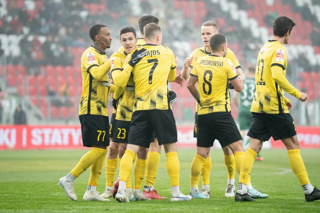 Wieczysta Kraków marzy o awansie do PKO BP Ekstraklasy Grupa piłkarzy w żółto-czarnych strojach świętuje zdobycie bramki na murawie stadionu, wokół widoczne trybuny z kibicami.