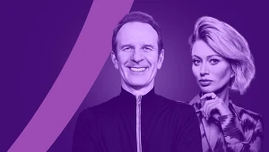 Uśmiechnięty mężczyzna stoi z przodu, ubrany w ciemną marynarkę z zamkiem, w tle kobieta z jasnymi włosami spoglądająca w bok, przytrzymująca palcami podbródek, całość w tonacji fioletowej z graficznym paskiem po lewej stronie.