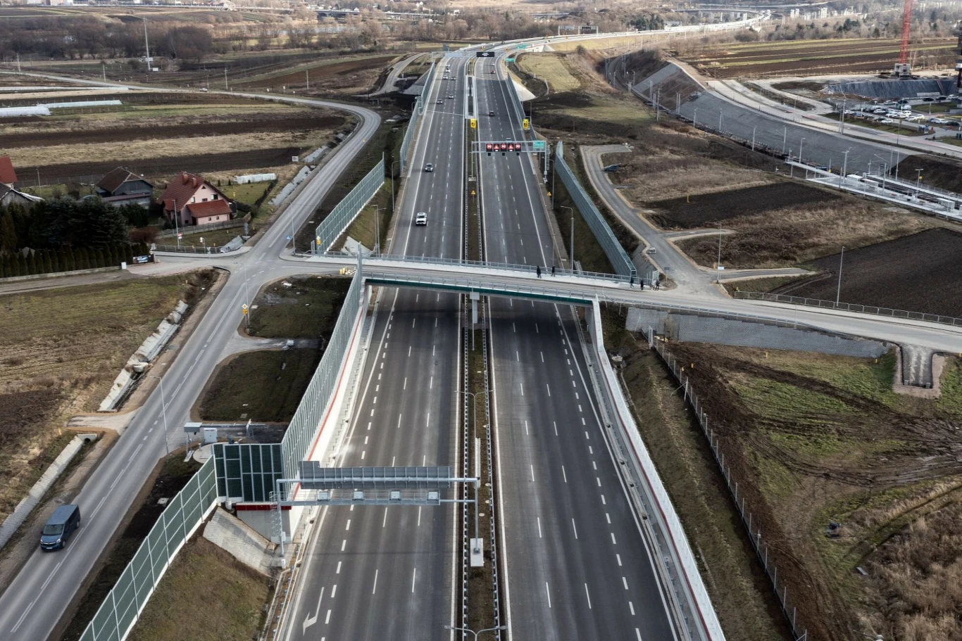 Rozbudowa sieci dróg szybkiego ruchu to główny powód spadku liczby wypadków Główna autostrada z betonowymi barierami, ekranami dźwiękochłonnymi i mostem przecinającym drogę, wokół tereny zielone i pojedyncze domy, widoczny minimalny ruch samochodowy.
