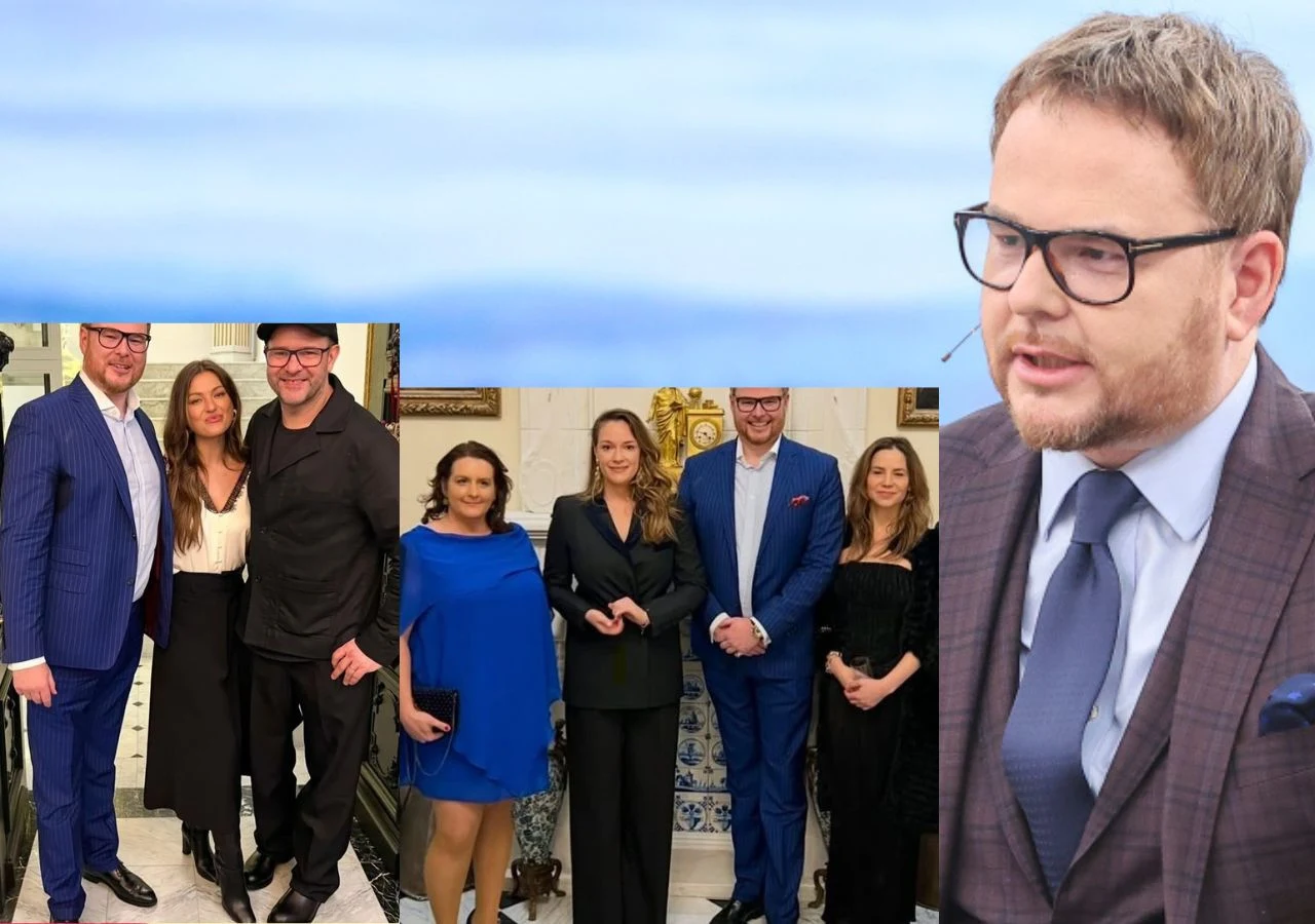 Grupa elegancko ubranych osób pozuje razem we wnętrzu urządzonym w klasycznym stylu, jedna osoba widoczna jest z bliższej perspektywy, ubrana w garnitur i okulary, patrząca w bok.