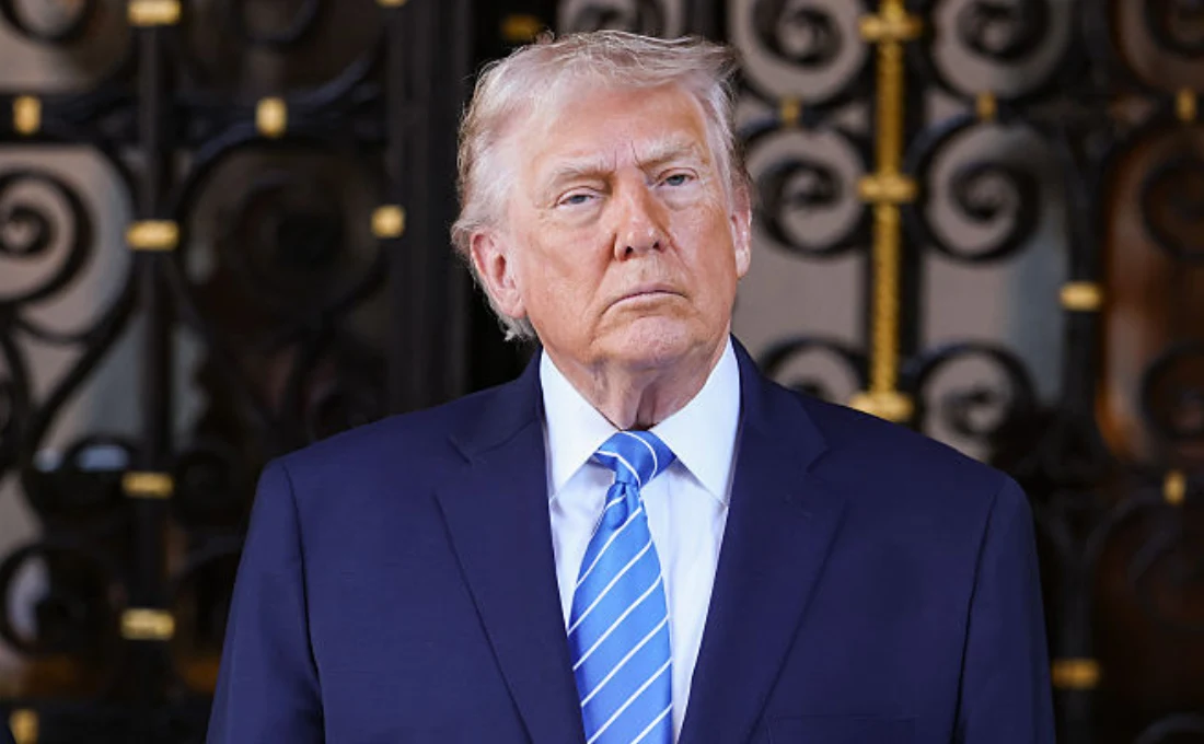 USA. Donald Trump ujawnił, że Władimir Putin poinformował go o ataku na jego rezydencję Starszy mężczyzna w garniturze i niebieskim krawacie stoi przed dekoracyjną, żelazną bramą, patrząc poważnie w stronę obiektywu.