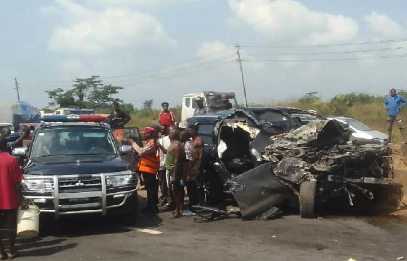 Powypadkowe wraki dwóch samochodów osobowych na drodze, zniszczone pojazdy otoczone przez ludzi, obecność radiowozu policyjnego oraz pracowników służb ratunkowych, którzy zabezpieczają miejsce zdarzenia.