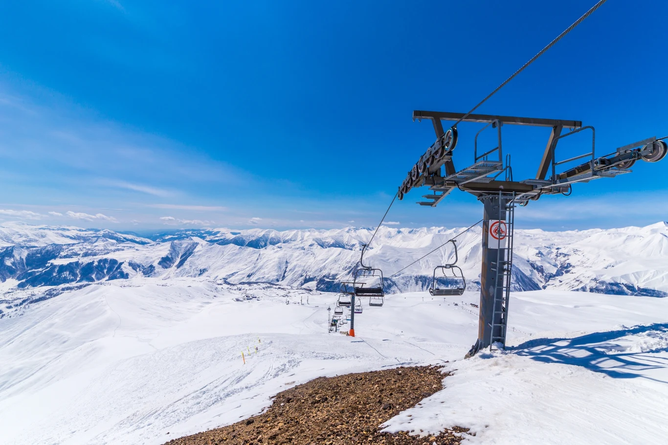Wyciąg narciarski na tle ośnieżonych gór i czystego, niebieskiego nieba, szerokie panoramy górskie oraz pusty stok.