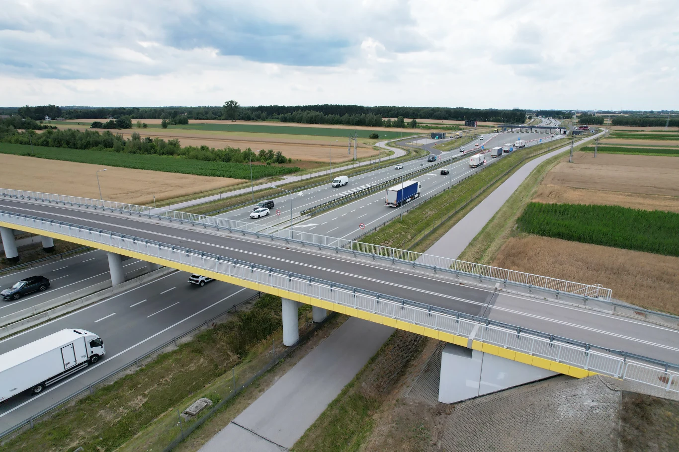 2,95 mld zł przeznaczył Krajowy Fundusz Drogowy w drugim kwartale 2026 na samą budowę dróg Autostrada przez pola, jadące samochody i ciężarówki, nowoczesny wiadukt, krajobraz wiejski z uprawami.