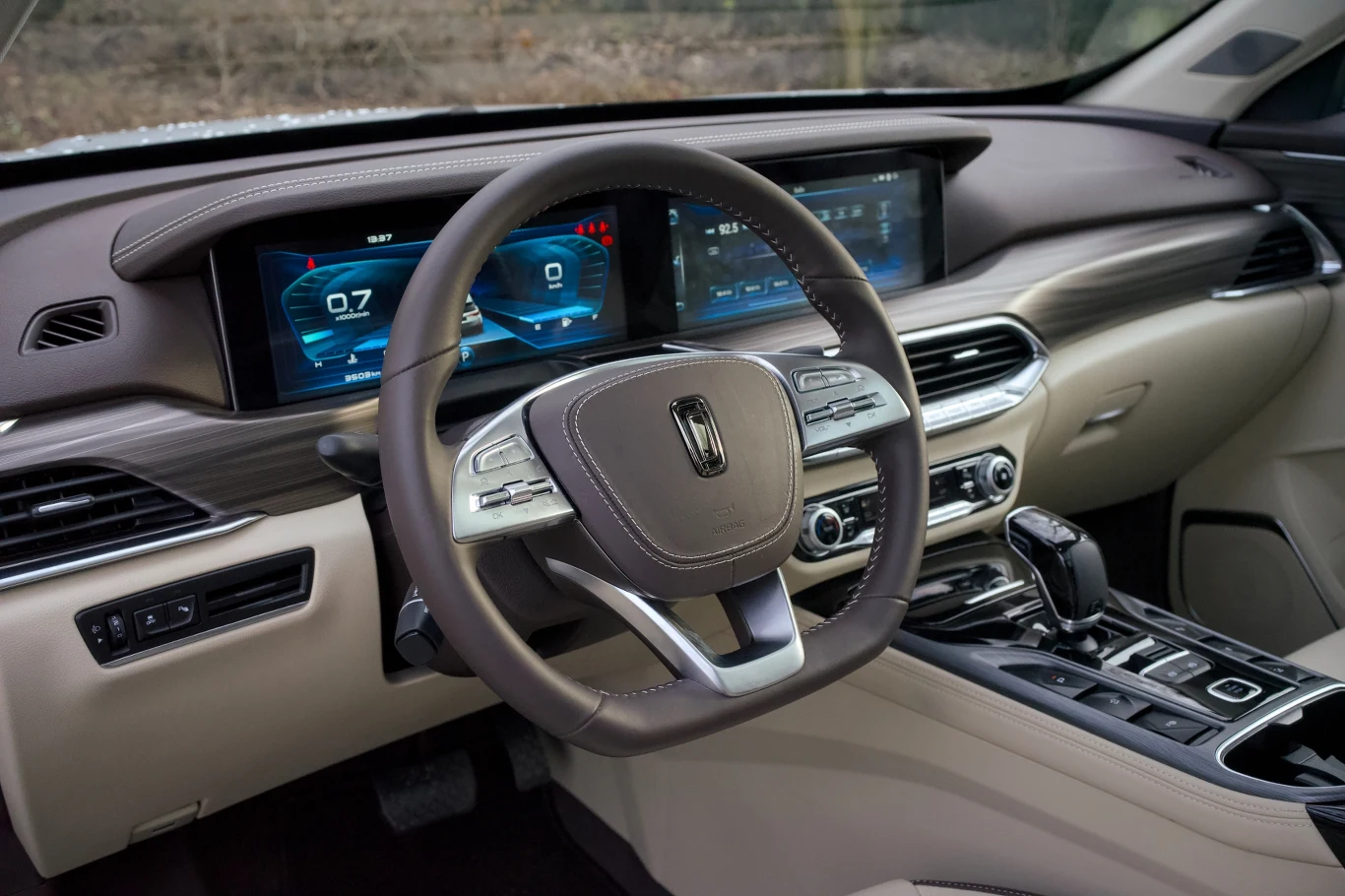 Luksusowe wnętrze samochodu z jasną tapicerką, centralnym podłokietnikiem, dużym ekranem dotykowym na konsoli środkowej oraz cyfrowymi wyświetlaczami przed kierowcą. Nowoczesna kierownica z elementami chromowanymi oraz ergonomicznie rozmieszczone przyc...