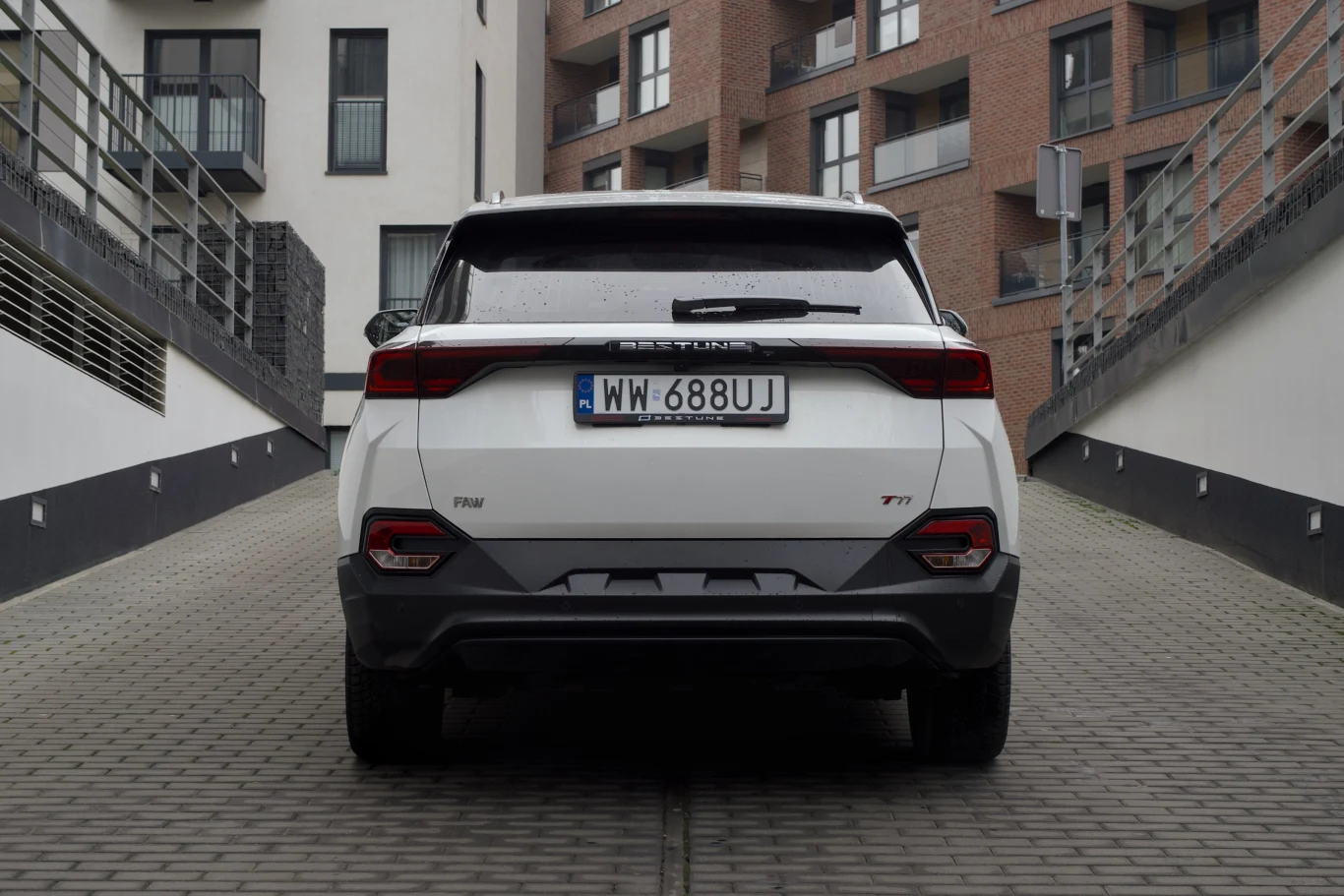 Biały samochód osobowy stojący tyłem na kostce brukowej pomiędzy nowoczesnymi budynkami mieszkalnymi. Na pojeździe widoczna polska tablica rejestracyjna, LED-owe tylne lampy i logo marki.