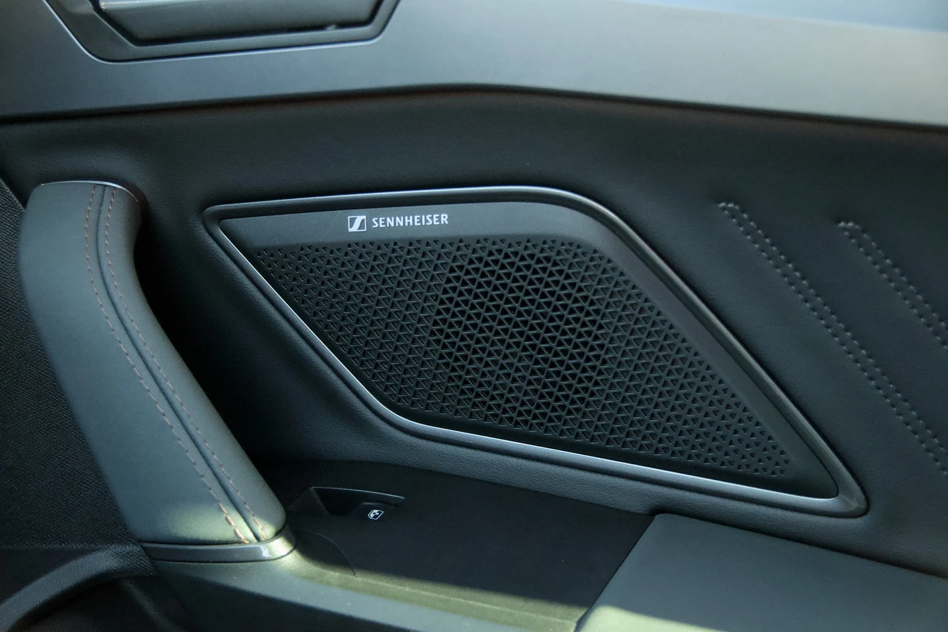 Panel drzwiowy samochodu z widocznym dużym głośnikiem marki Sennheiser oraz fragmentem tapicerki i przeszyć na boczku.
