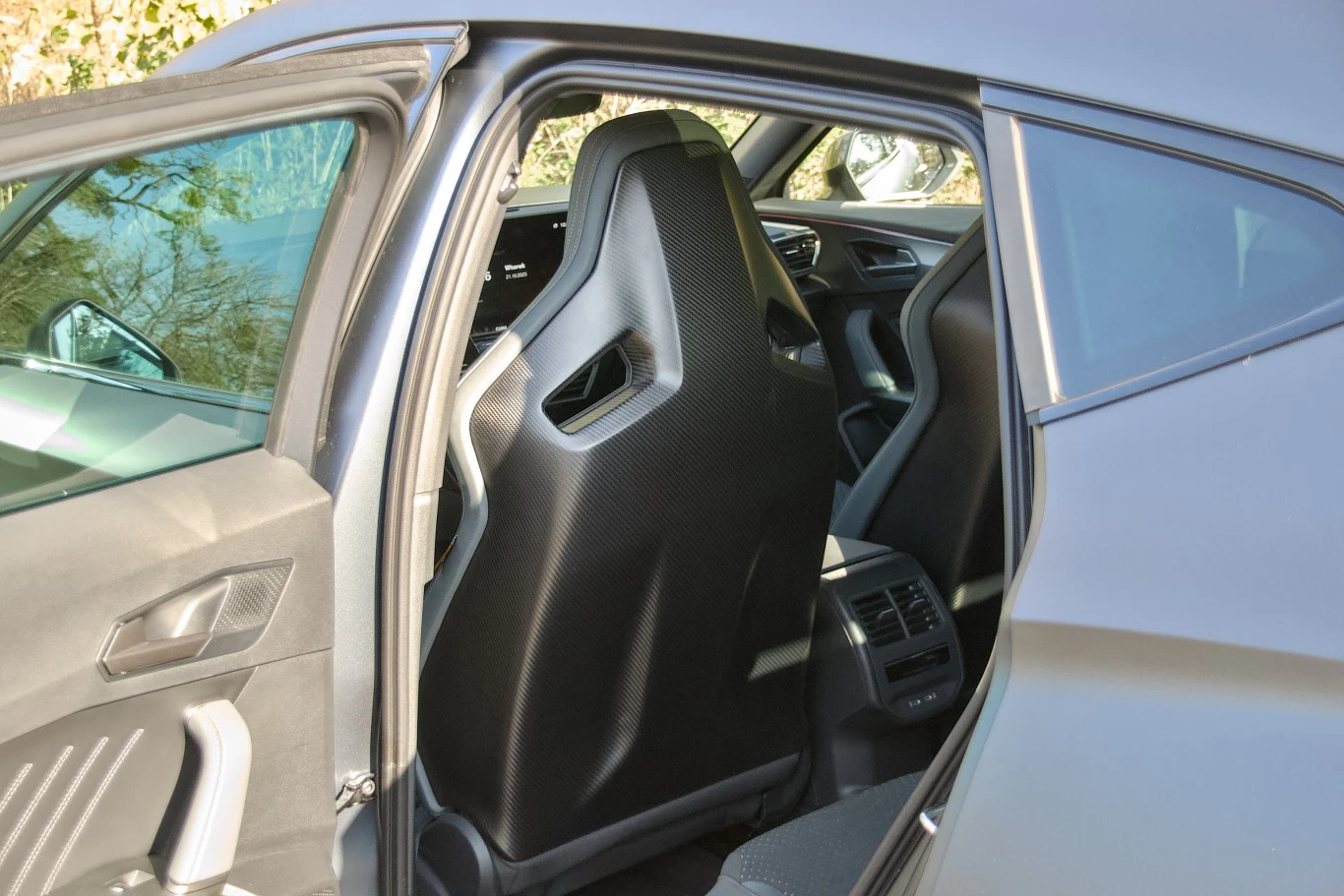 Wnętrze samochodu z widokiem na tylne siedzenia, przednie fotele kubełkowe z czarnym wykończeniem oraz widocznym panelem klimatyzacji dla pasażerów z tyłu.