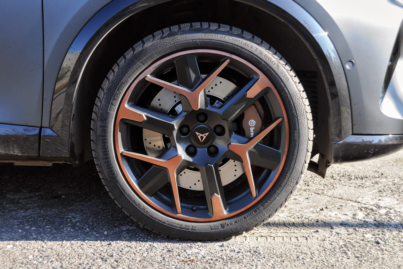 Felga aluminiowa w kolorze czarno-miedzianym z wyraźnym logo marki Cupra, zamontowana na nowoczesnych hamulcach tarczowych samochodu, powierzchnia asfaltowa wokół