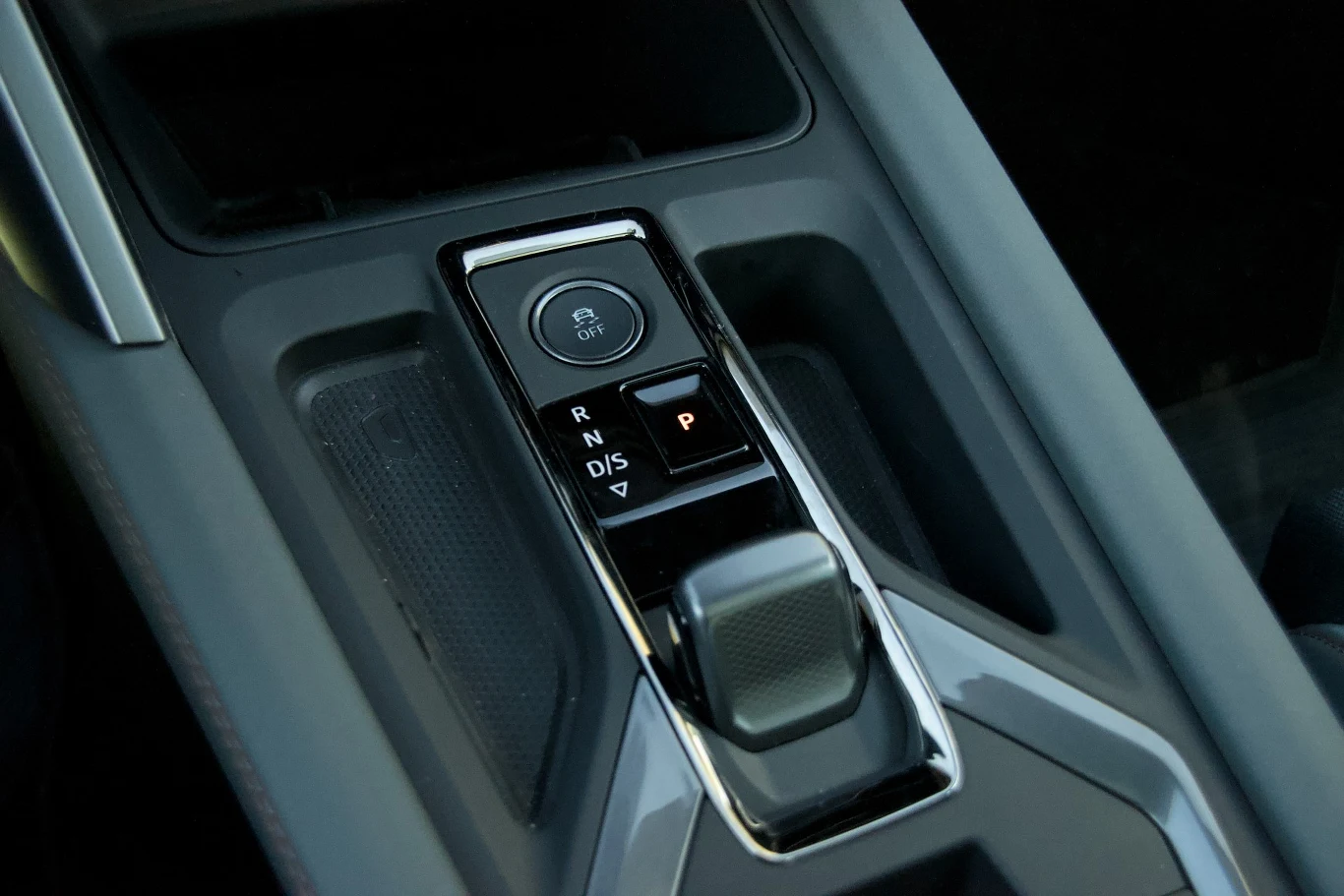 Panel środkowy nowoczesnego samochodu z elektroniczną dźwignią zmiany biegów, przyciskiem do sterowania trybami jazdy i funkcją hamulca postojowego.