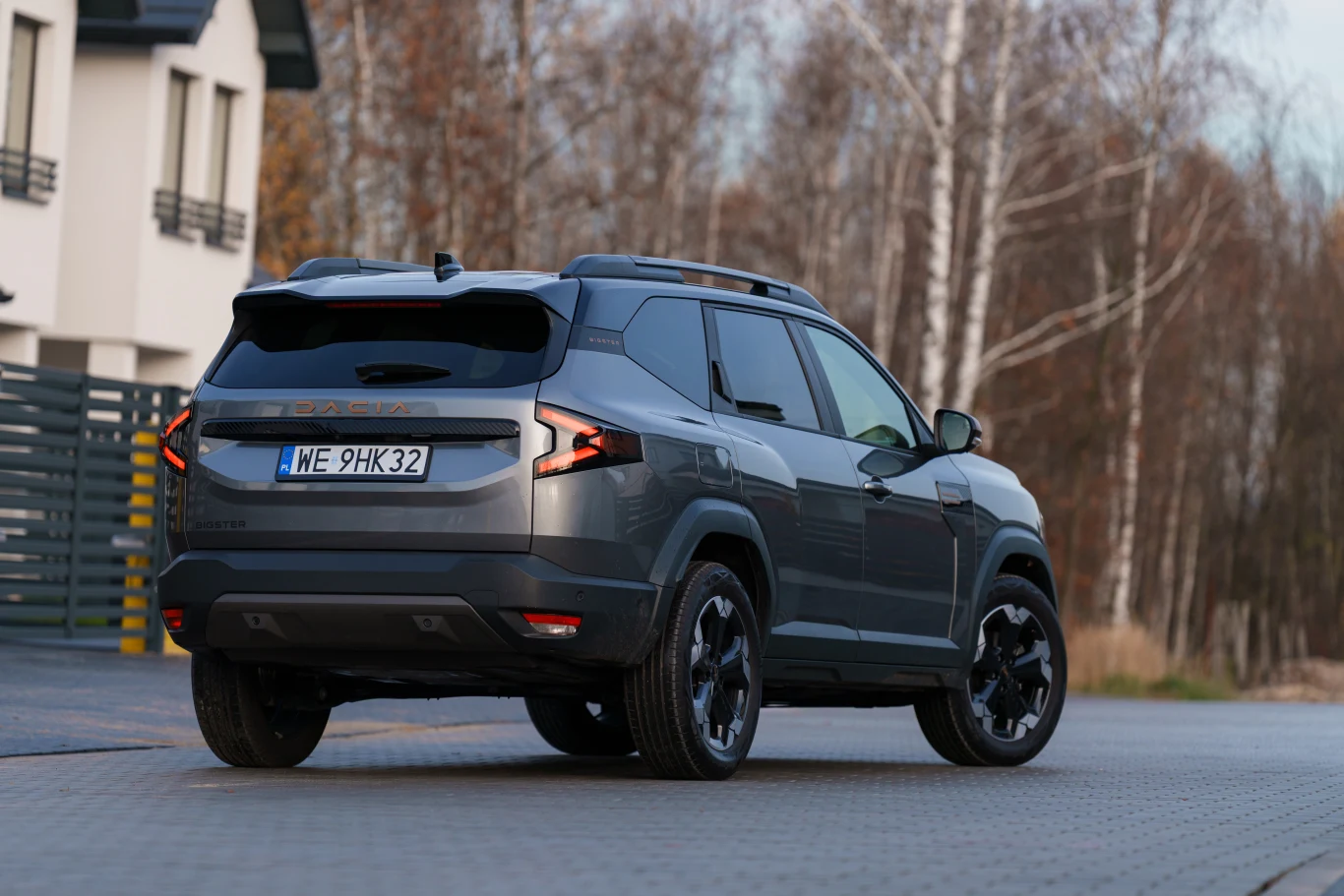 Szary SUV nowoczesnej marki zaparkowany na ulicy osiedlowej, w tle widoczny fragment budynku mieszkalnego oraz drzewa bez liści.