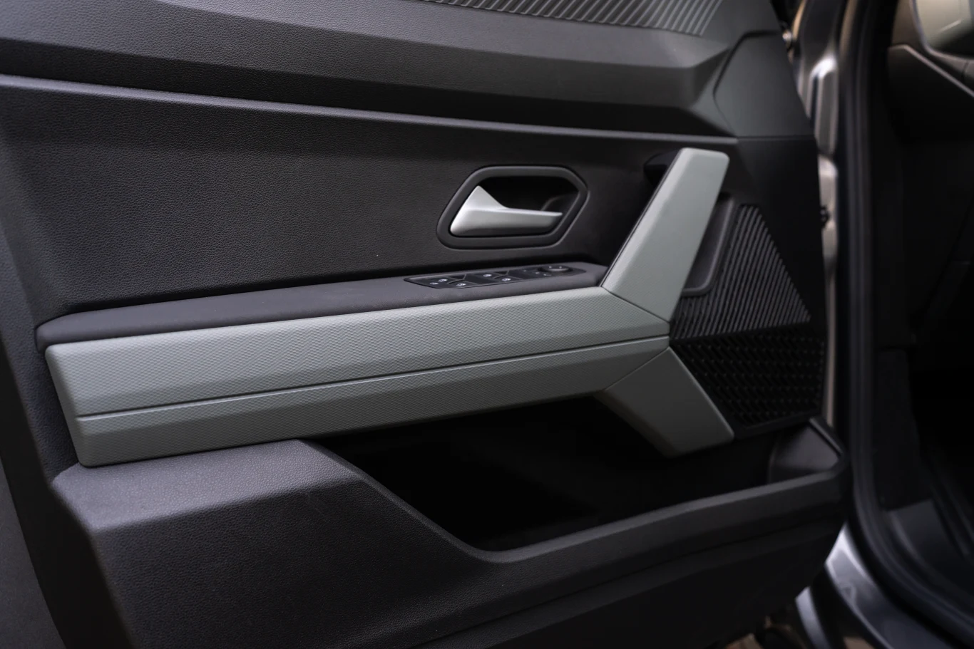 Wnętrze drzwi samochodu z widocznym uchwytem, przyciskami sterowania szybami oraz czarną i szarą tapicerką.