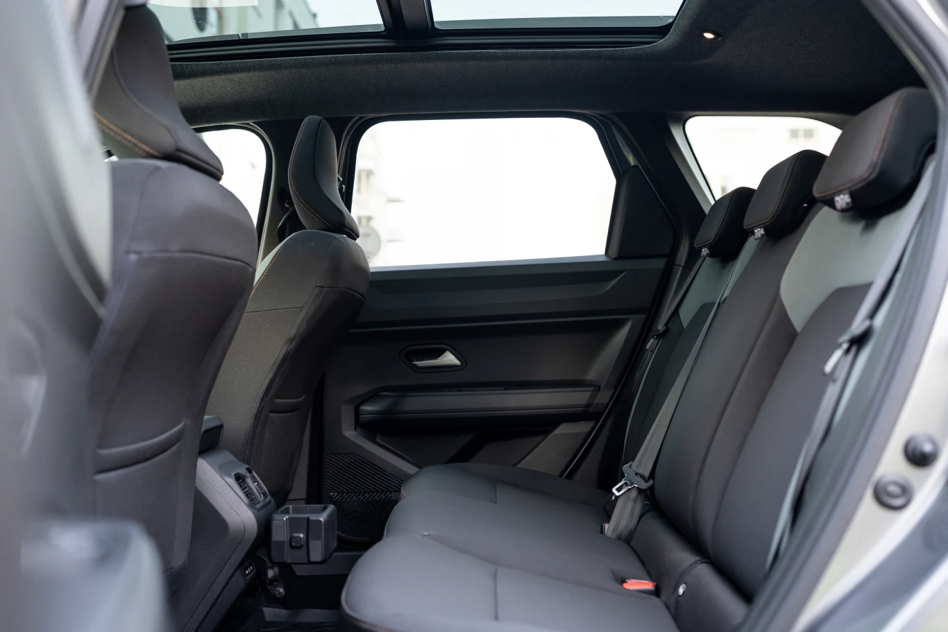 Drugi rząd siedzeń w samochodzie osobowym, tapicerka w ciemnym kolorze, przestronne wnętrze z widocznym panoramicznym oknem dachowym, dobrze utrzymane siedzenia z zagłówkami i zapiętymi pasami bezpieczeństwa.