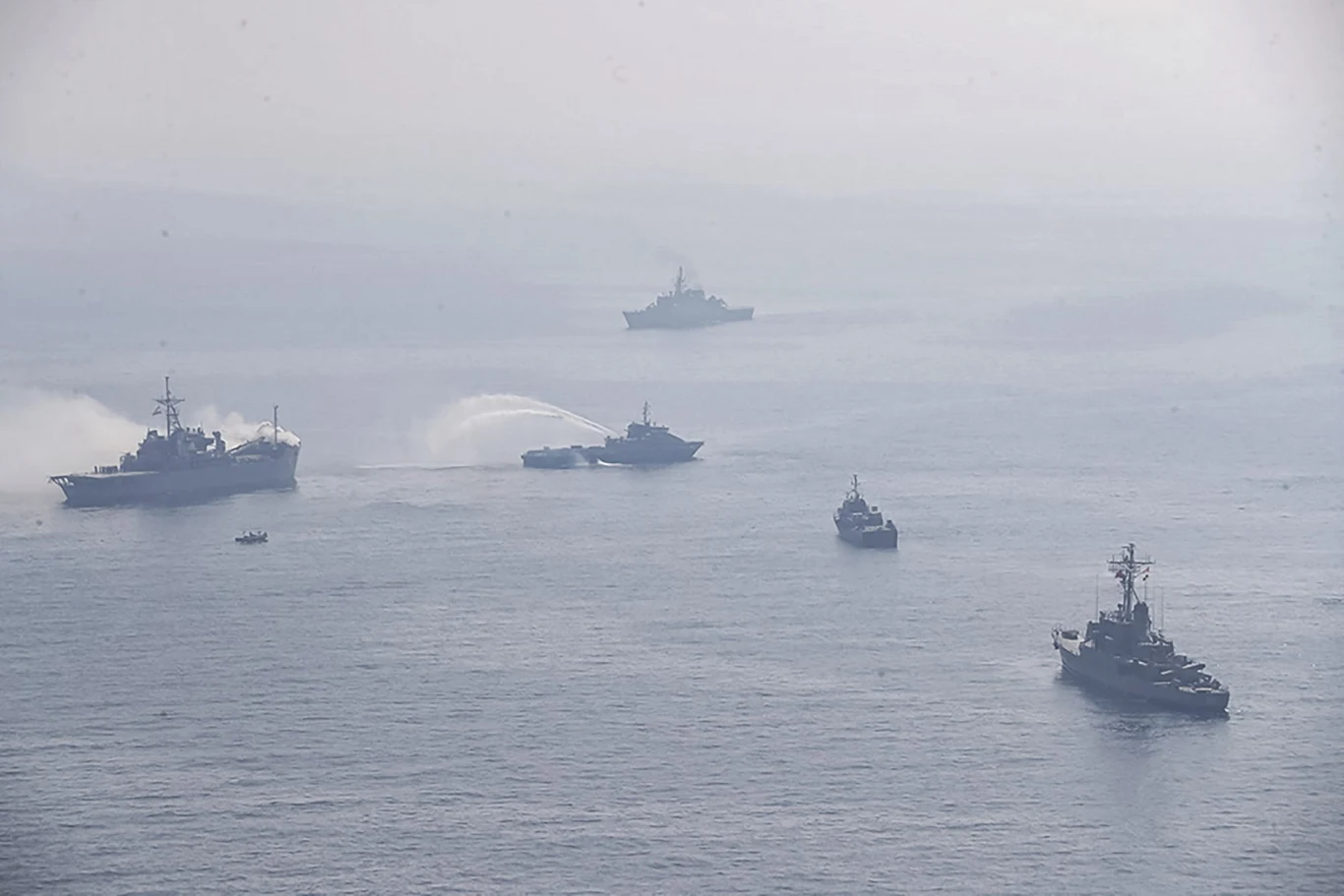 Rosyjsko-irańskie manewry przeprowadzone w 2021 roku. Teraz do wspólnych ćwiczeń dołączyli Chińczycy Grupa okrętów wojennych płynących po spokojnej powierzchni morza, niektóre jednostki wytwarzają widoczne smugi wody, całość spowita jest lekką mgłą