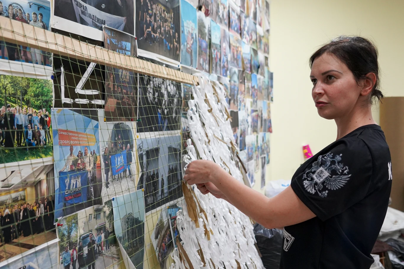 Kobieta pracująca przy dużej siatce, na której zamieszczone są zdjęcia różnych grup i wydarzeń, układa materiał na siatce w pomieszczeniu z jasnym oświetleniem.