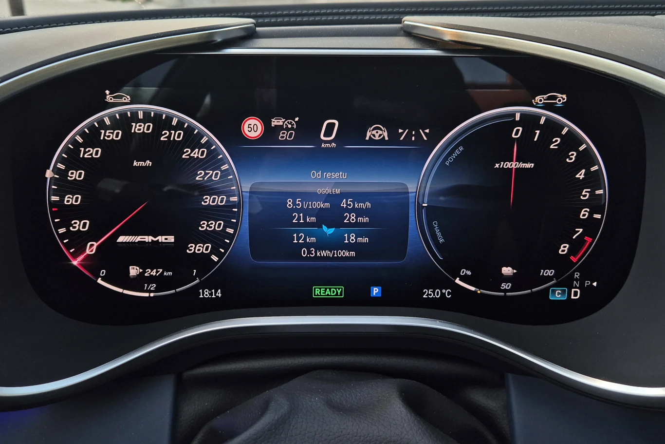 Cyfrowy wyświetlacz zestawu wskaźników samochodu z widocznymi informacjami o prędkości, obrotach silnika, zużyciu paliwa, zasięgu i wskazaniach systemów pokładowych. Z lewej strony duży prędkościomierz, z prawej obrotomierz. Pośrodku ekran z informacją...