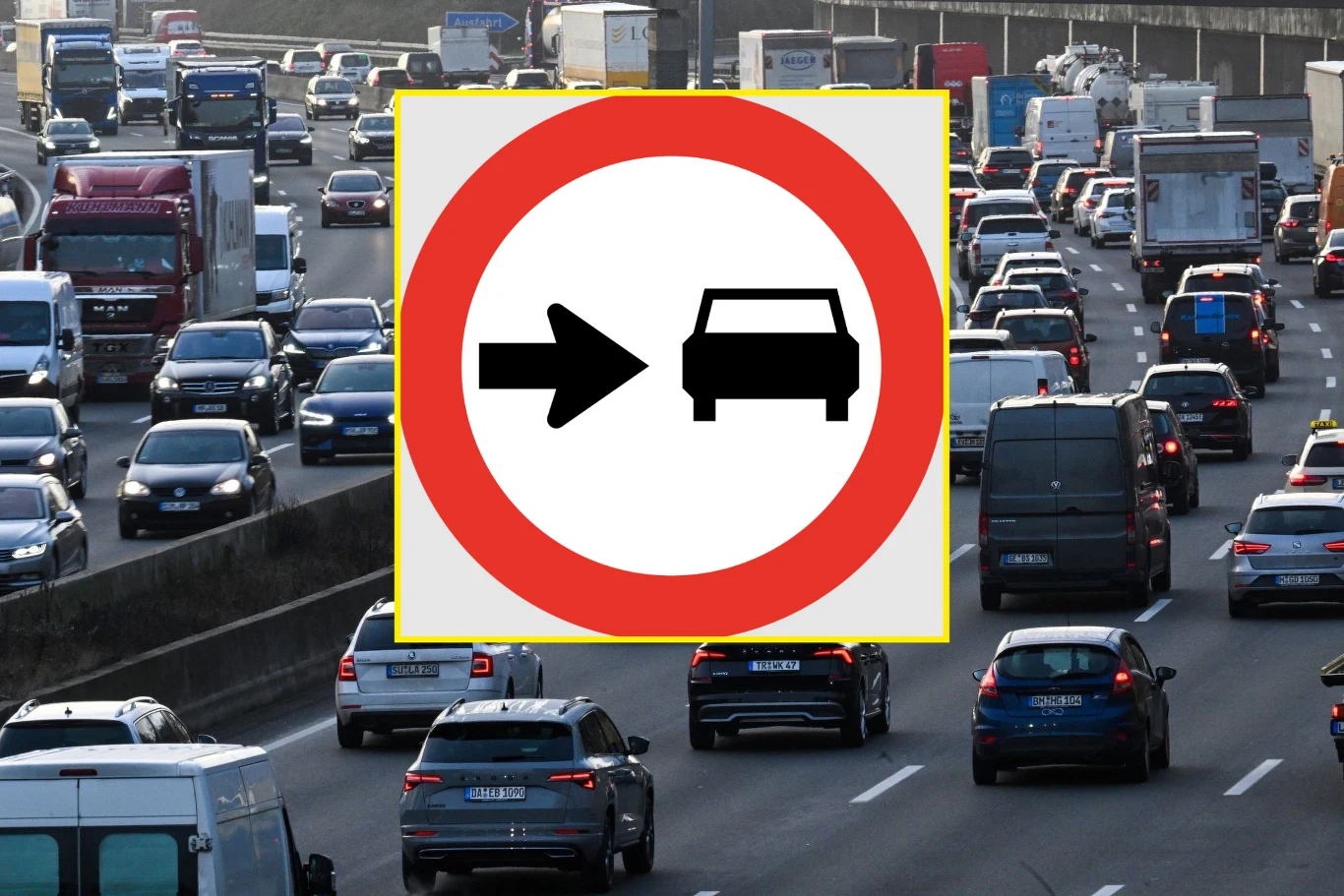 Co oznacza znak ze strzałką skierowaną w stronę samochodu? / Fot. Wikimedia Commons Zakorkowana autostrada w godzinach szczytu, wiele samochodów oraz pojazdów ciężarowych stojących na kilku pasach ruchu, na pierwszym planie znak zakazu wjazdu pojazdów silnikowych.