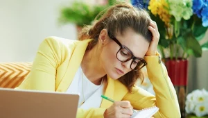 Kobieta w okularach, siedzi na kanapie, robi notatki, planuje rok