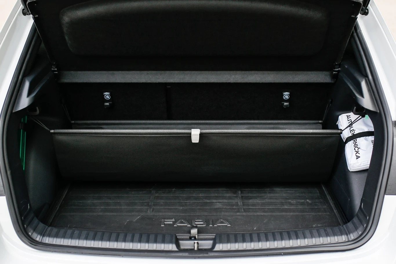 Otwarty bagażnik samochodu osobowego z wyraźnie widoczną matą ochronną z napisem Fabia, po prawej stronie znajduje się niewielka torba z logo producenta.