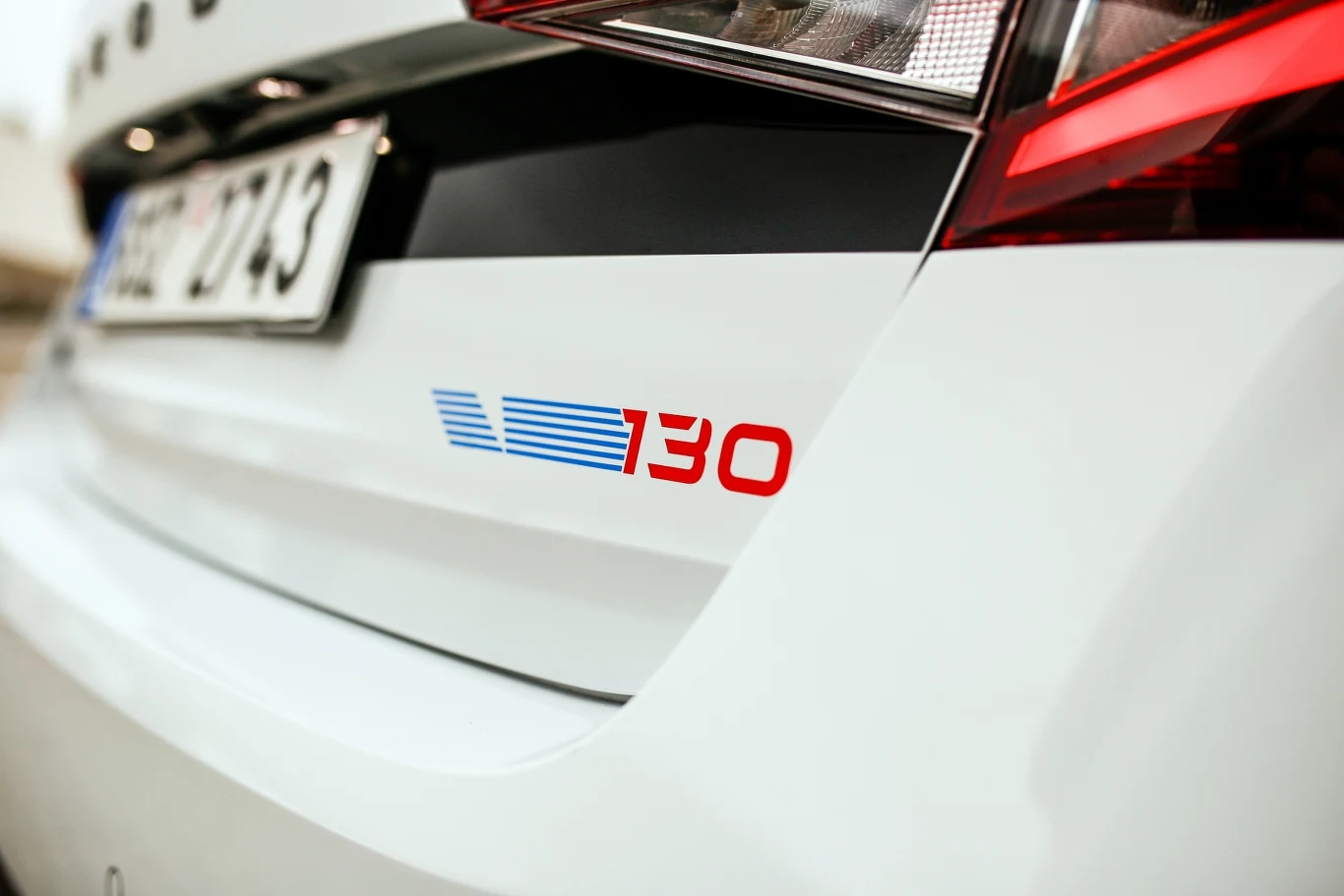 Biała karoseria samochodu z widocznym oznaczeniem modelu w postaci liczby 130 w kolorze niebieskim i czerwonym oraz fragment tylnego światła i tablicy rejestracyjnej.
