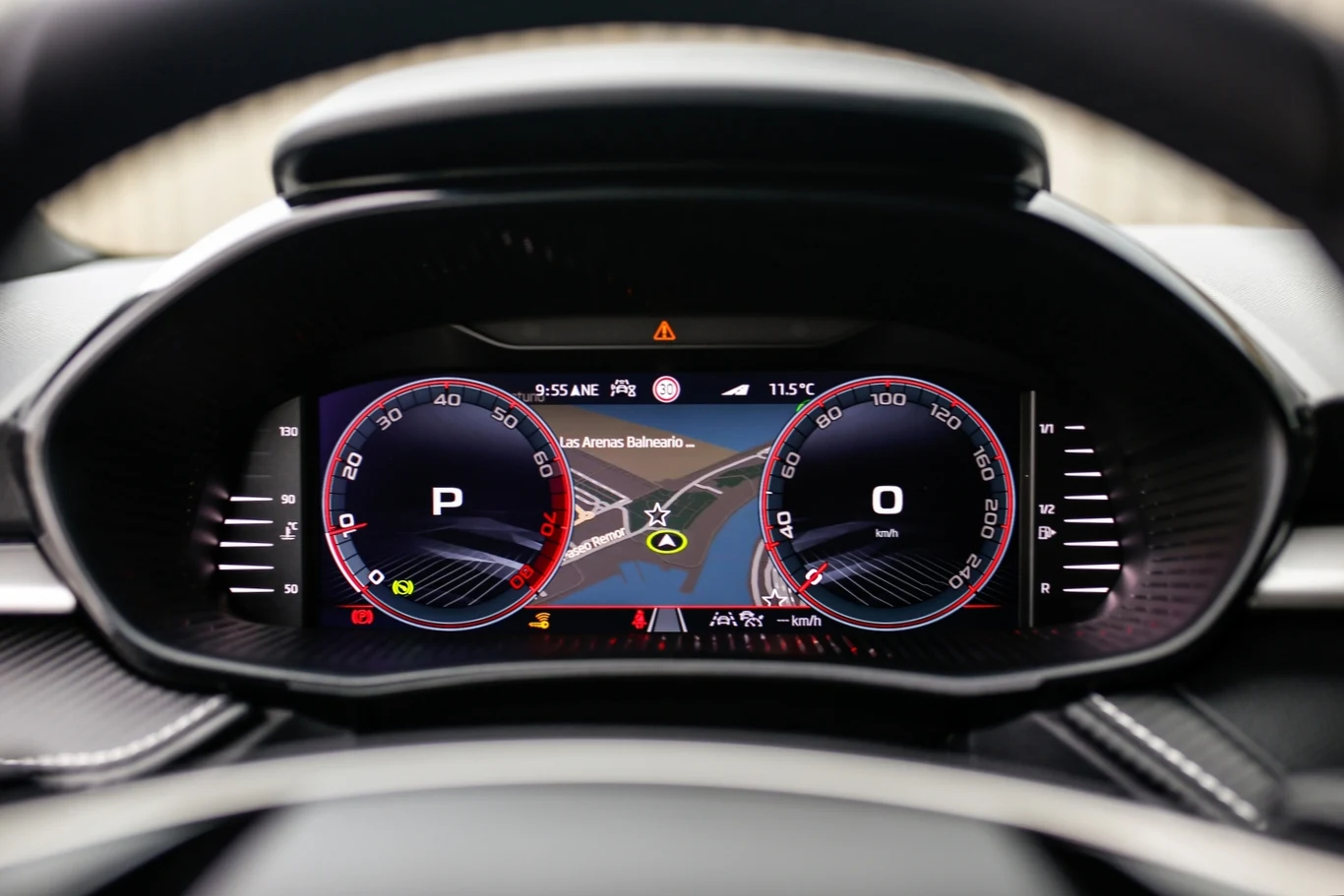 Cyfrowy wyświetlacz zestawu wskaźników w nowoczesnym samochodzie, z cyfrowym prędkościomierzem, informacją o pozycji skrzyni biegów, szczegółową mapą nawigacji oraz dodatkowymi ikonami informacyjnymi.