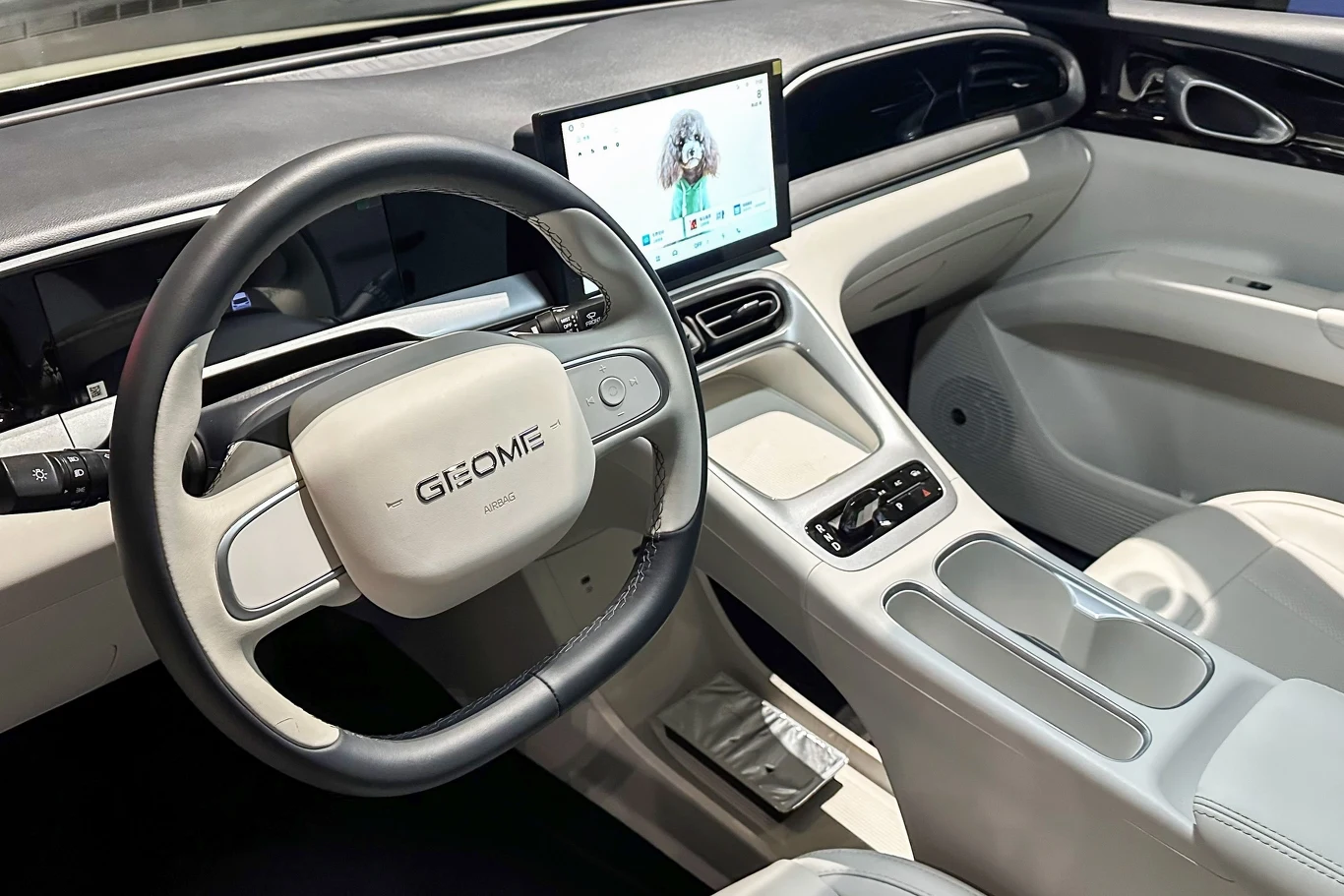 Nowoczesne wnętrze samochodu marki GEOME z dużym ekranem dotykowym na konsoli centralnej, białą tapicerką i minimalistycznym designem deski rozdzielczej.