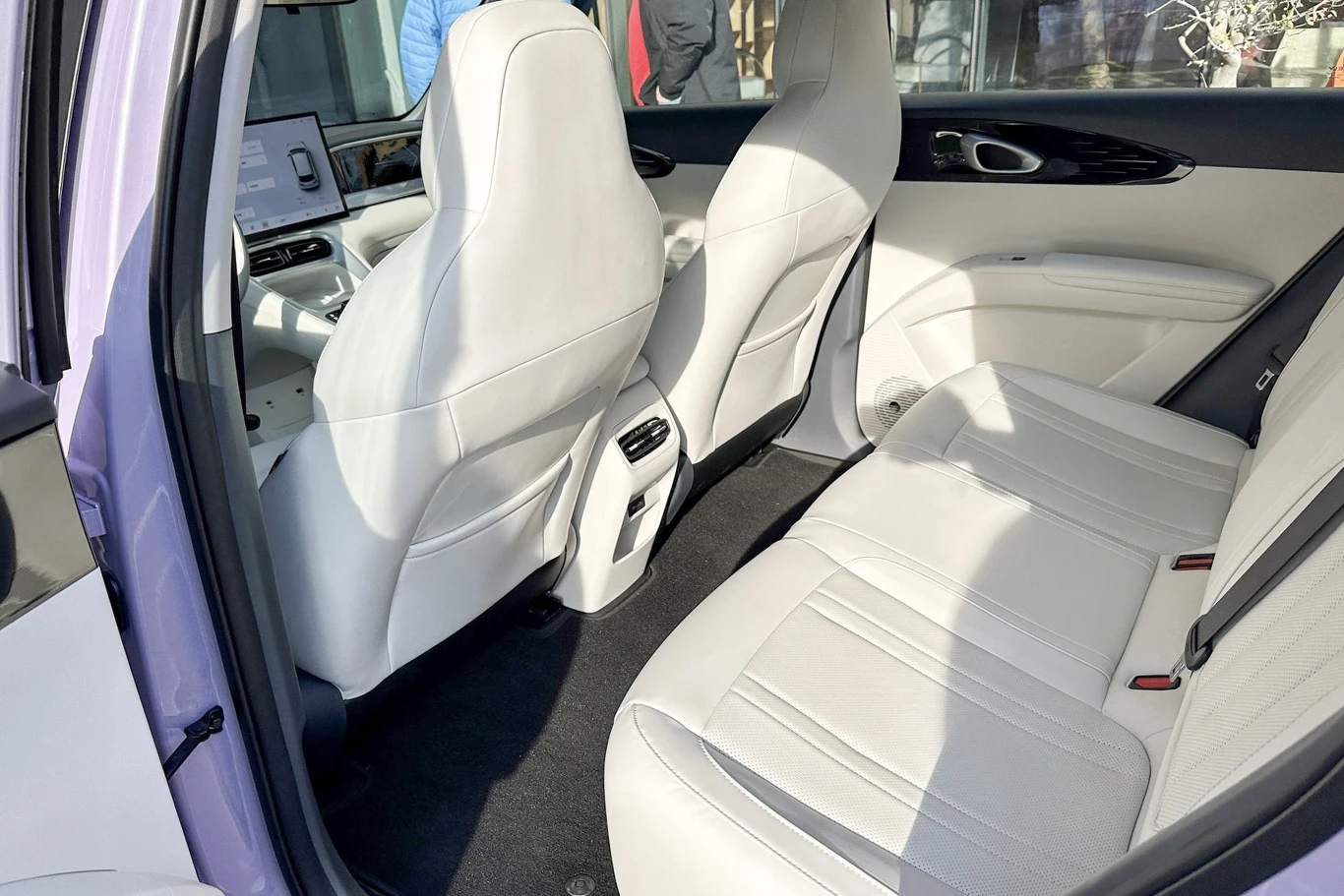 Wnętrze samochodu z białą, skórzaną tapicerką, wygodnymi siedzeniami oraz nowoczesnym panelem sterowania widocznym z przodu. Jasne wnętrze sprawia wrażenie przestronnego i eleganckiego.