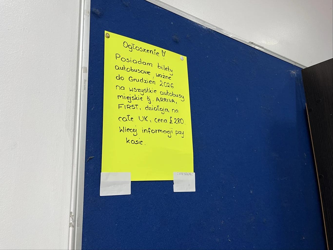Ogłoszenie o kupnie biletów na angielskie autobusy Jaskrawożółta kartka z ręcznie napisanym ogłoszeniem na niebieskiej tablicy korkowej. Ogłoszenie dotyczy biletów autobusowych ważnych do grudnia 2026 roku na wszystkie autobusy miejskie, z informacją o cenie i miejscu uzyskania szczegółów. Kartka jest ...