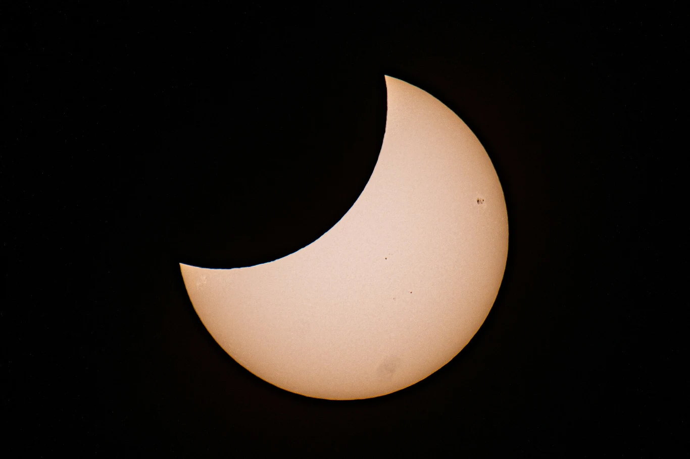 Częściowo przesłonięta tarcza słoneczna z ciemnym wycinkiem księżyca wchodzącym na powierzchnię Słońca, na tle czarnego nieba.