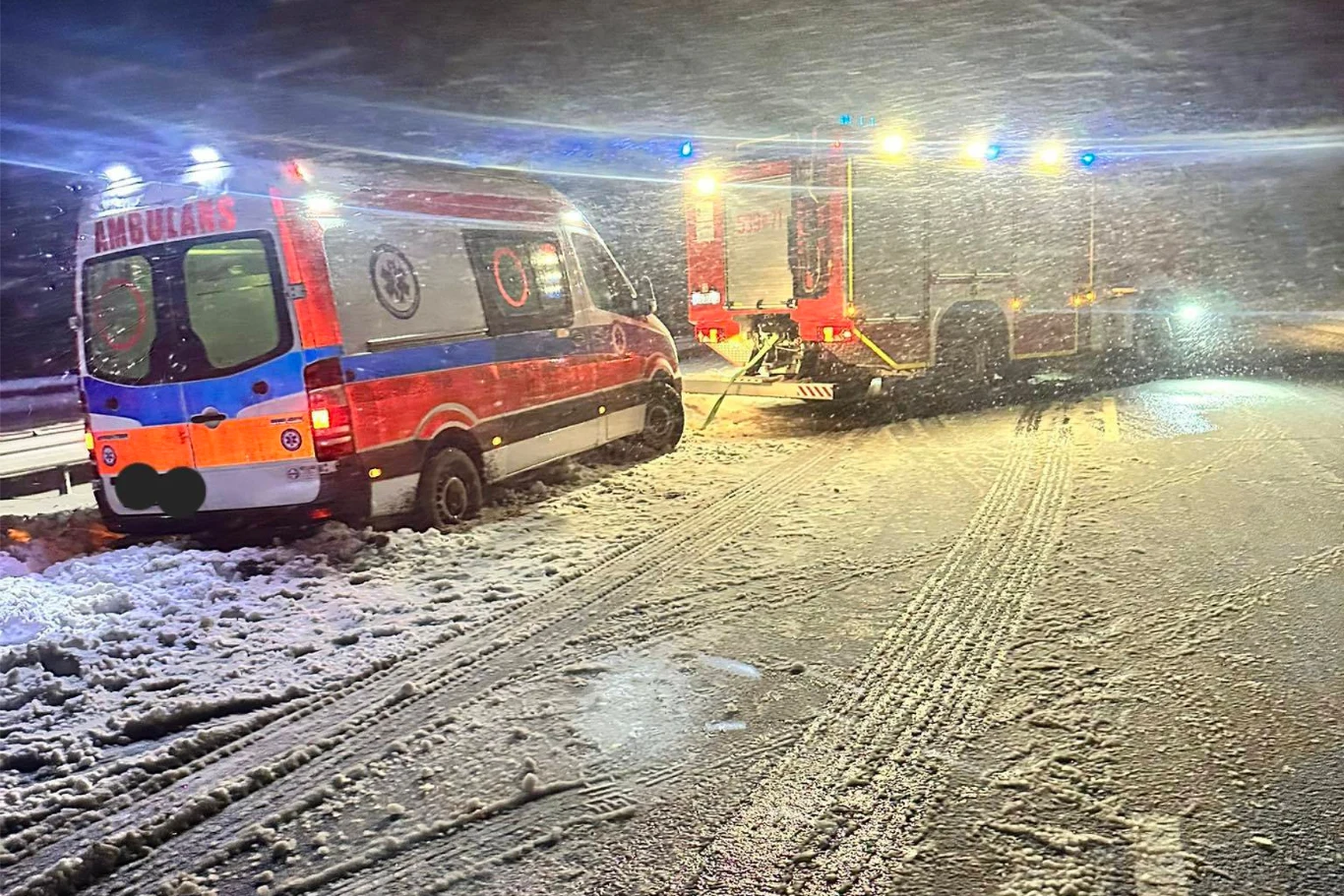 Kartki utknęły w zaspach. Na pomoc ruszyli strażacy, mieszkańcy i rolnik. / Fot. Facebook - OSP KSRG Małdyty Ambulans oraz wóz strażacki zatrzymane na ośnieżonej drodze podczas intensywnych opadów śniegu. Jednostki ratownicze oświetlone światłami sygnalizacyjnymi, widoczne ślady opon na jezdni, ciemne warunki nocne.