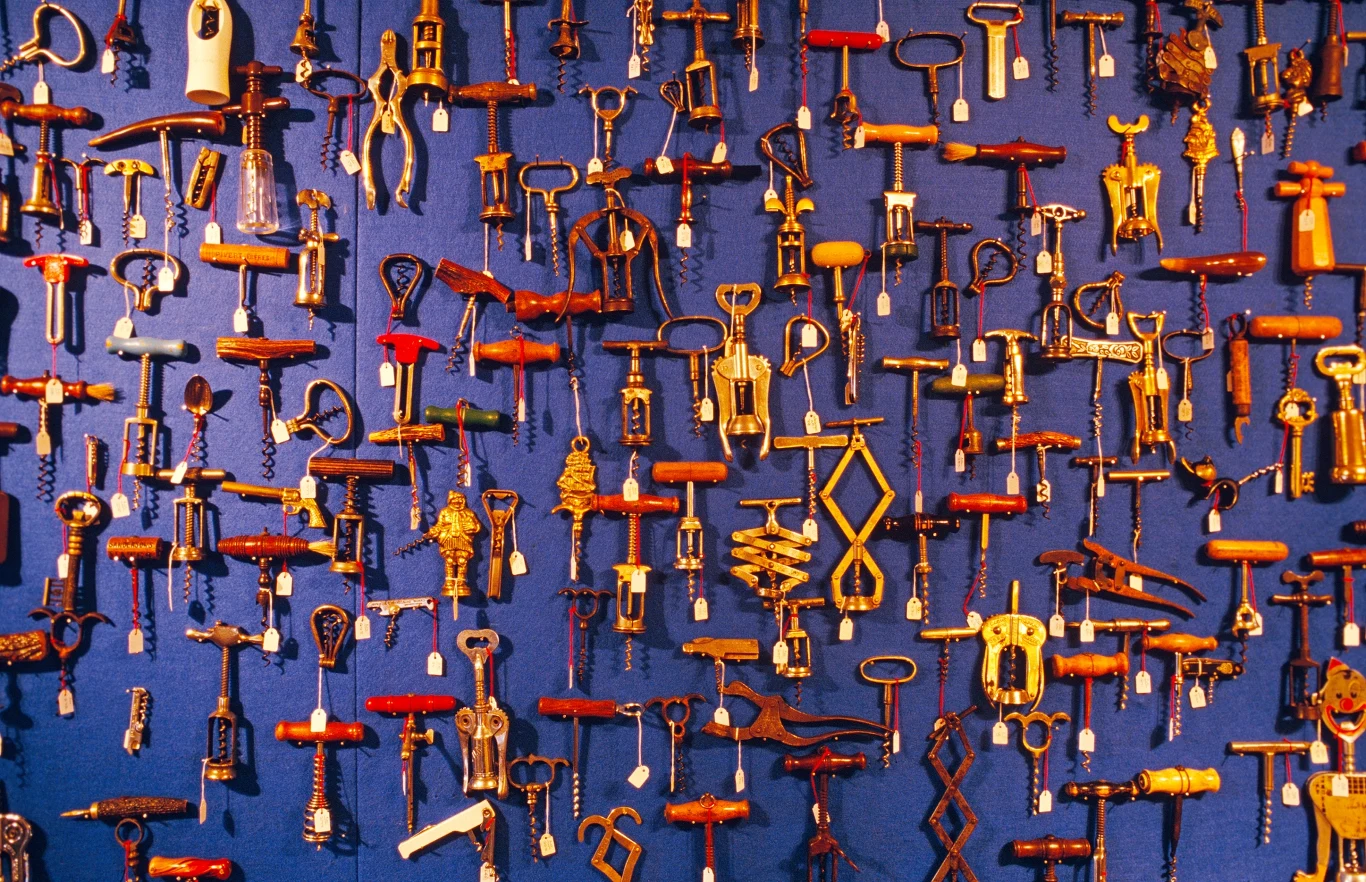 Stare korkociągi. Kolekcja różnorodnych korkociągów o różnych kształtach i wzorach zawieszonych na niebieskim tle, pokazująca różnorodność i unikalność każdego egzemplarza.