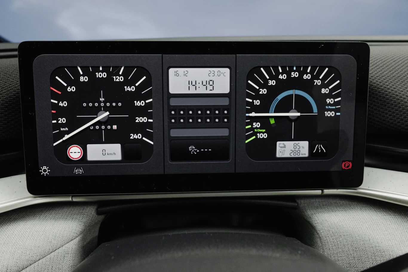 Cyfrowy wyświetlacz samochodu z trzema głównymi wskaźnikami: prędkościomierz po lewej, zegar oraz wyświetlacz temperatury i daty pośrodku, wskaźnik mocy i poziomu naładowania akumulatora po prawej.