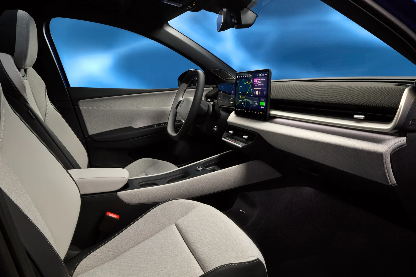 Nowoczesne, minimalistyczne wnętrze samochodu z jasnymi fotelami, dużym ekranem multimedialnym na konsoli centralnej, elegancką deską rozdzielczą oraz panoramicznym widokiem na zewnątrz.