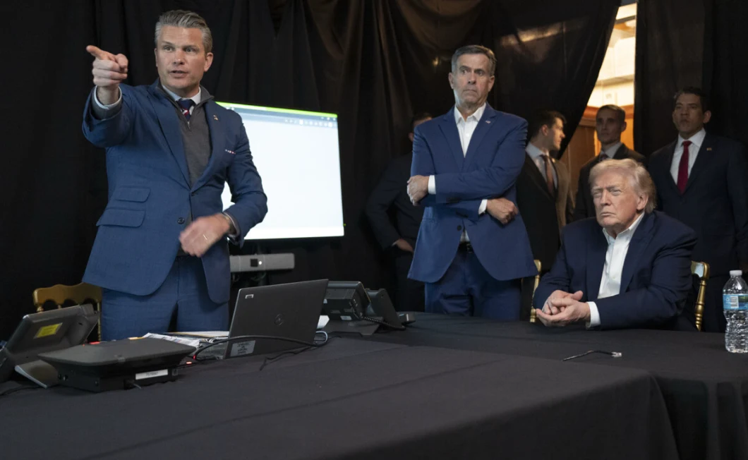 Pete Hegseth obserwował w specjalnej kwaterze atak USA w Wenezueli Grupa mężczyzn w garniturach zgromadzona przy stole konferencyjnym, na którym znajdują się telefony i sprzęt elektroniczny, jeden z mężczyzn energicznie wskazuje kierunek, pozostali obserwują sytuację z uwagą, w tle widoczny ekran projekcyjny oraz ciem...