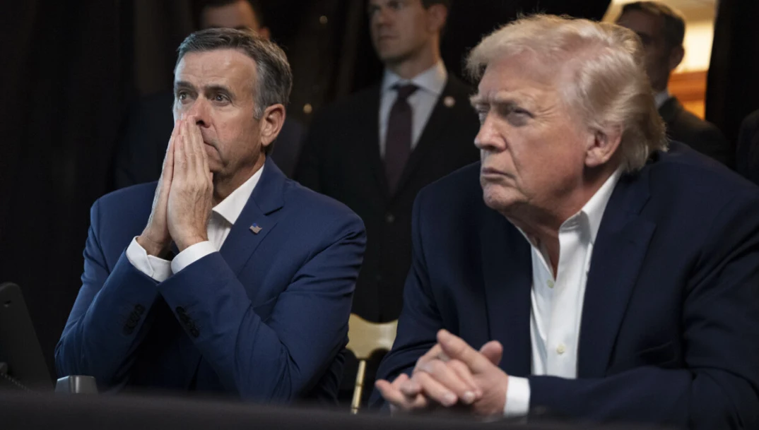 Dyrektor CIA i prezydent USA obserwują akcję pojmania Nicolasa Maduro Dwóch mężczyzn w garniturach siedzi obok siebie, wyraża skupienie i napięcie, jeden z nich opiera dłonie o twarz, obok znajduje się drugi, obserwujący coś poza kadrem. W tle widoczne są sylwetki kilku osób w formalnych strojach.