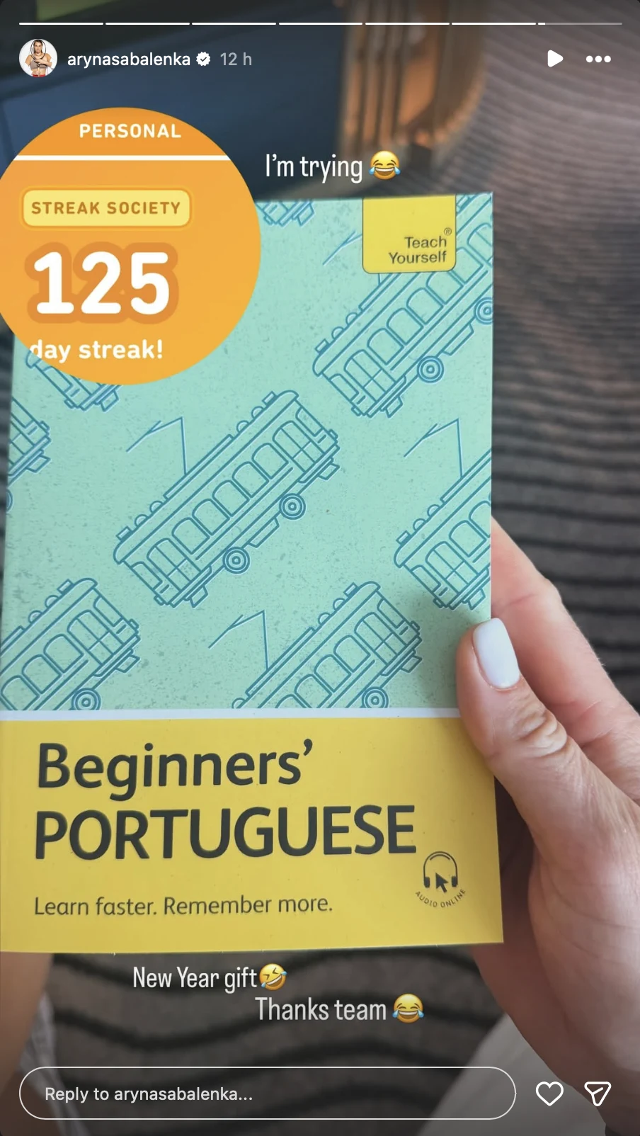 Dłoń trzyma książkę do nauki języka portugalskiego dla początkujących z żółto-niebieską okładką ozdobioną ilustracjami tramwaju. Na okładce znajdują się napisy motywujące dotyczące nauki oraz informacja o 125-dniowej serii nauki.