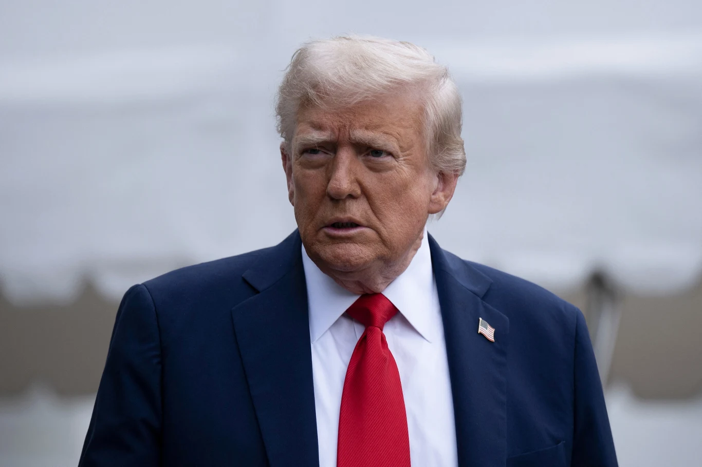 Pomysł Donalda Trumpa na zmuszenie firm - za pomocą ceł - do przeniesienia produkcji do USA nie powiódł się Mężczyzna w średnim wieku o jasnych włosach ubrany w garnitur, białą koszulę i czerwoną krawat, stoi na zewnątrz na neutralnym tle.