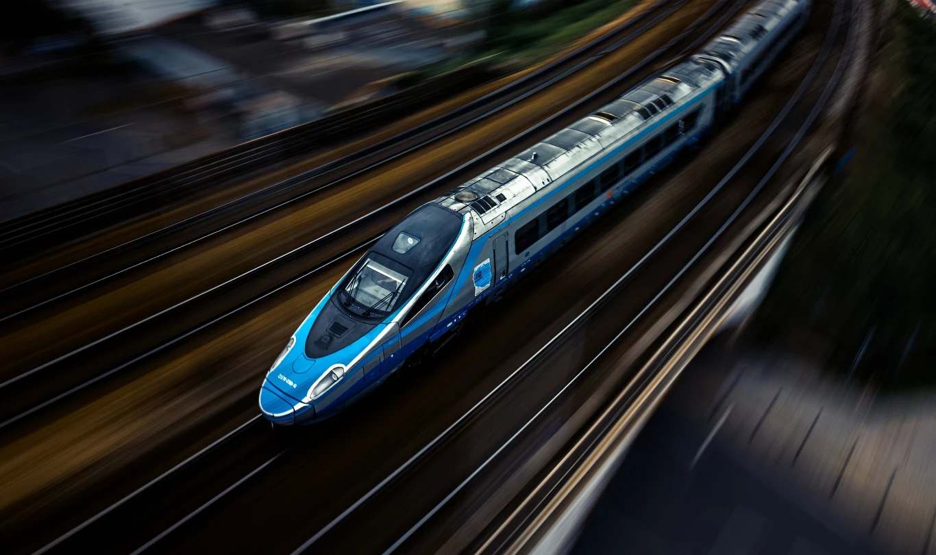 Nowoczesny niebieski pociąg porusza się z dużą prędkością po torach, dynamiczne rozmycie tła podkreśla szybki ruch pojazdu.