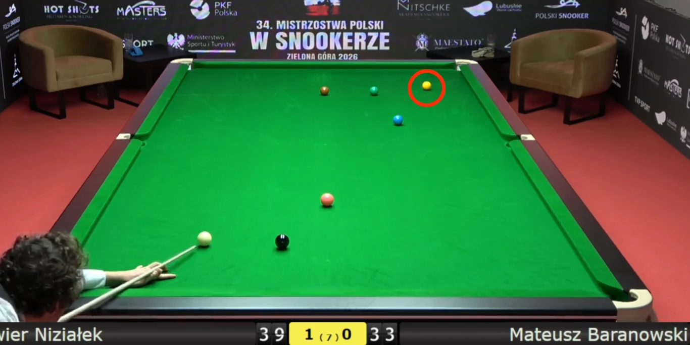 Zawodnik przygotowujący się do uderzenia w bilę na stole bilardowym podczas mistrzostw Polski w snookerze, widoczne kolorowe bile, plansza wyników oraz elementy wyposażenia sali turniejowej.