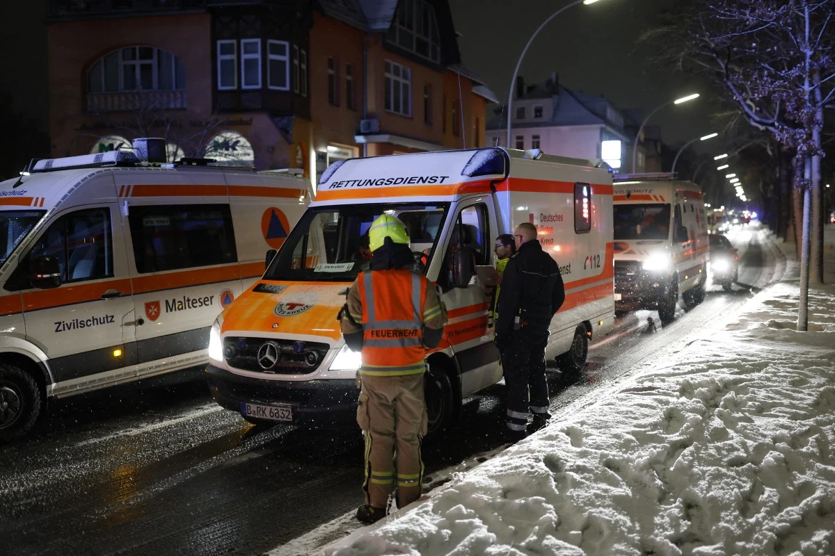 Poważna awaria w Berlinie. Kilkadziesiąt tysięcy gospodarstw nie ma prądu Kolumna karetek pogotowia zaparkowana wzdłuż ośnieżonej ulicy, ratownicy medyczni i strażacy stojący obok pojazdów, nocna sceneria, światła pojazdów odbijające się od śniegu, otoczenie zabudowy miejskiej.