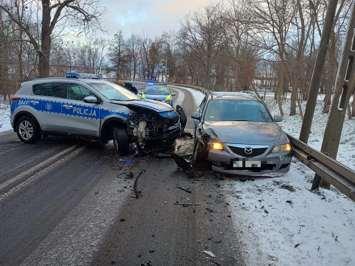 Pijany kierowca Mazdy podczas ucieczki przed policją zderzył się z radiowozem Dwa rozbite samochody, w tym radiowóz policyjny i srebrny samochód osobowy, stoją na zaśnieżonej drodze w lesistej okolicy. Widać uszkodzenia przodu obu pojazdów, rozrzucone części oraz policyjne światła sygnalizacyjne.