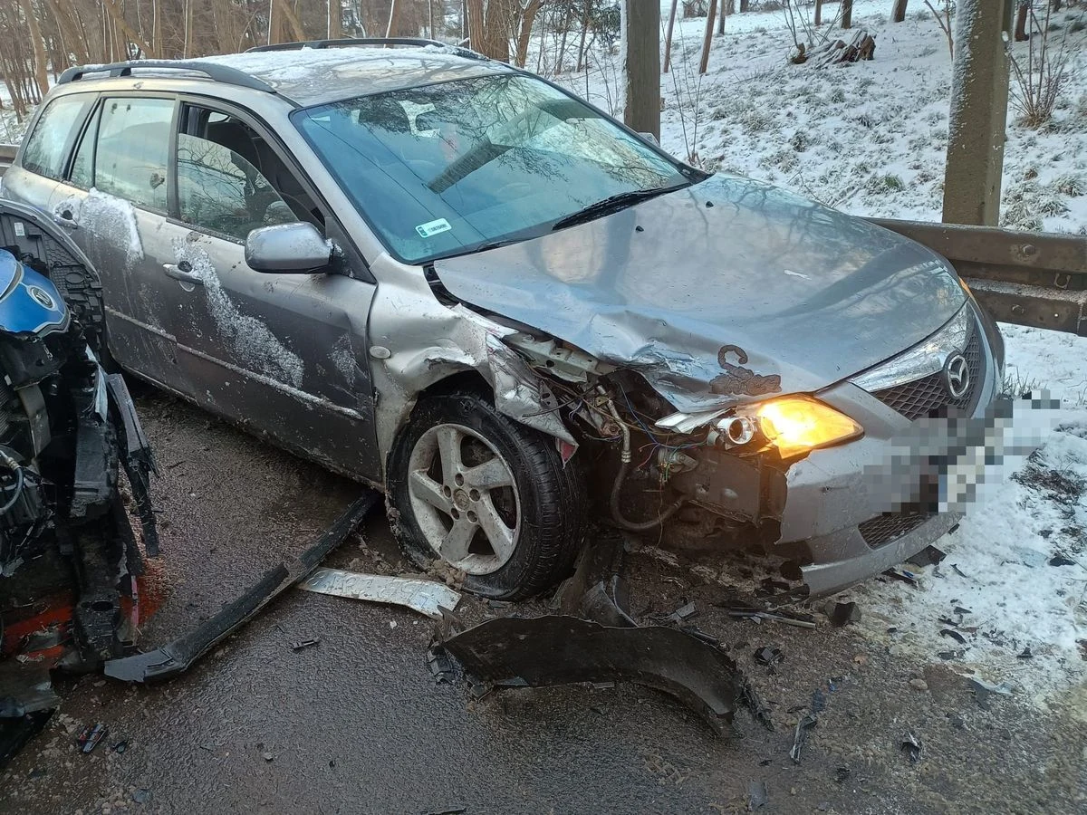 Według policji Mazda 6 była uszkodzona jeszcze przed interwencją Rozbity samochód osobowy marki Mazda z poważnie uszkodzonym przednim lewym błotnikiem i zderzakiem stoi na zimowej, pokrytej śniegiem drodze. W tle drewniana bariera oraz drzewa porośnięte śniegiem. Obok widoczne części innego pojazdu uczestniczącego w...