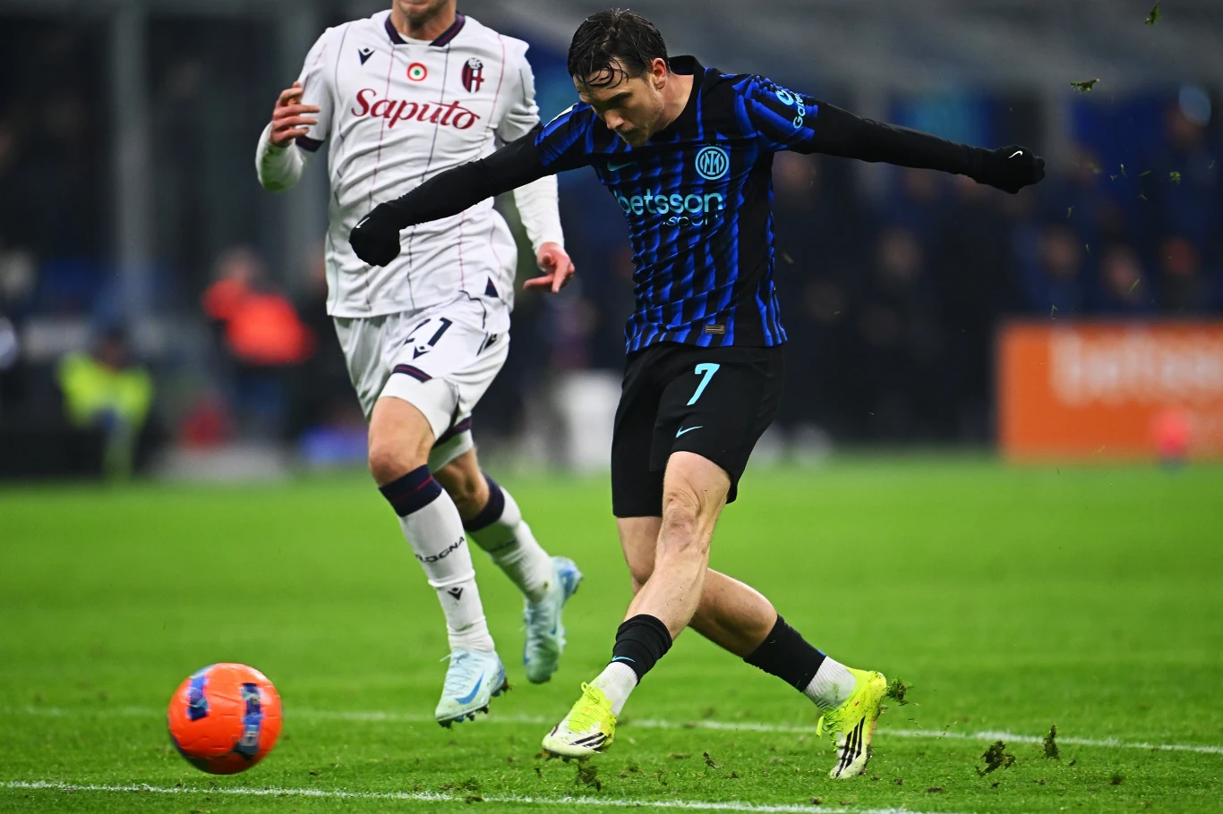 Zawodnik w niebiesko-czarnej koszulce drużyny Inter Mediolan wykonuje strzał na bramkę podczas meczu piłki nożnej, gracz drużyny przeciwnej w białym stroju próbuje blokować futbolistę