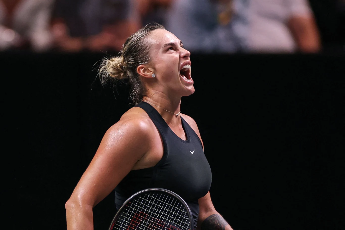 Aryna Sabalenka rywalizowała z Cristiną Bucsą w drugiej rundzie WTA 500 w Brisbane Tenisistka w czarnym stroju sportowym krzycząca z wyrazem intensywnych emocji, trzymająca rakietę tenisową na tle rozmytego, ciemnego tła.