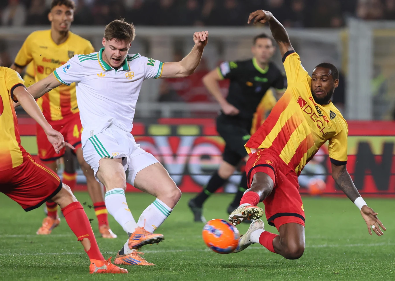 W taki sposób Evan Ferguson (w białym stroju) otworzył wynik spotkania Piłkarze dwóch drużyn rywalizują o piłkę podczas meczu, zawodnik w żółto-czerwonym stroju wykonuje wślizg próbując odebrać piłkę rywalowi w białym stroju, wokół nich widoczni są inni zawodnicy oraz sędzia.