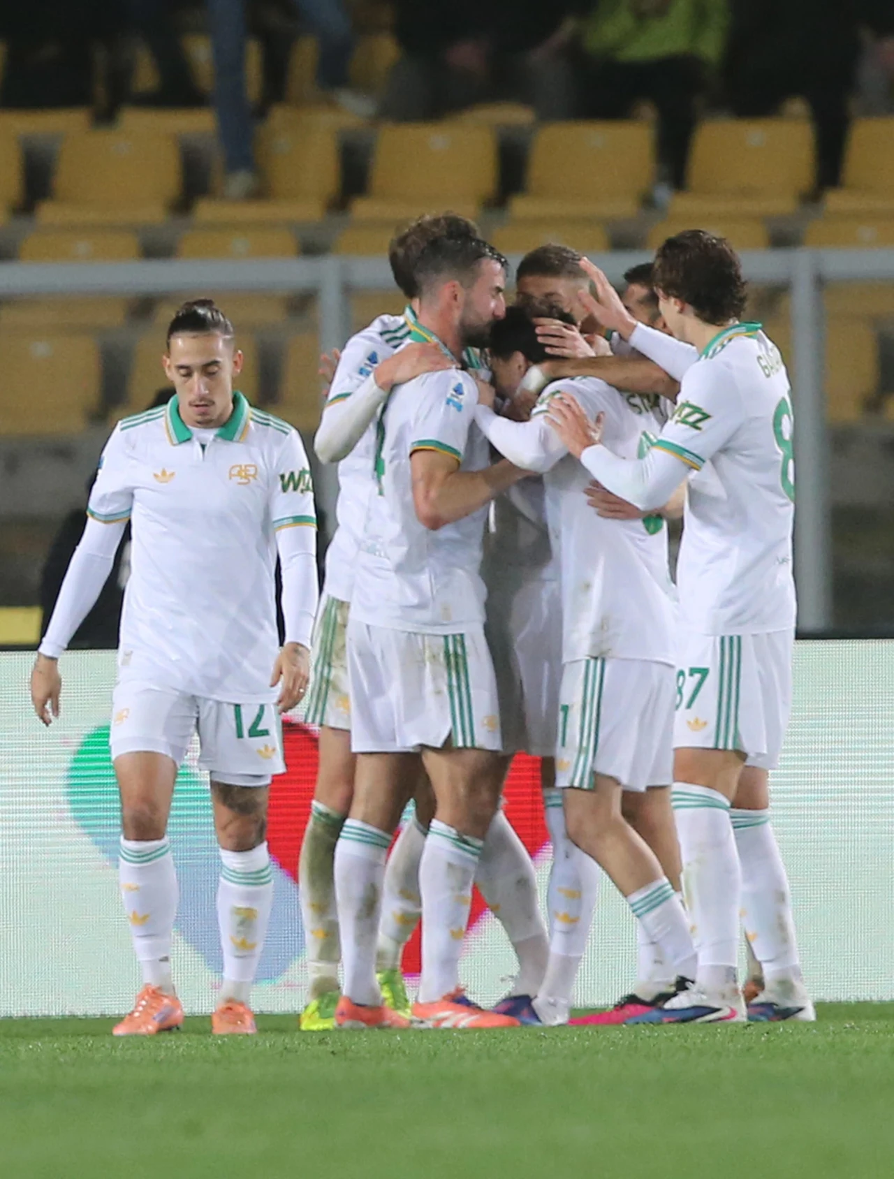 Po bramce wprowadzonego z ławki Artema Dowbyka rzymianie byli już pewni swego Grupa piłkarzy ubranych w białe stroje z zielonymi akcentami świętuje zdobycie gola podczas meczu na stadionie, wokół nich puste żółte krzesełka trybun.