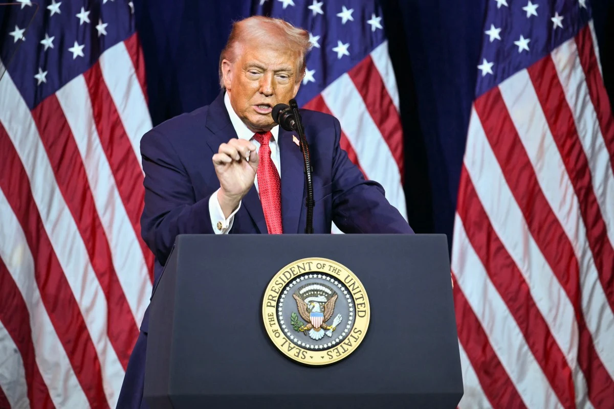 Prezydent USA Donald Trump Donald Trump przemawia zza mównicy z pieczęcią prezydenta USA, w tle amerykańskie flagi.
